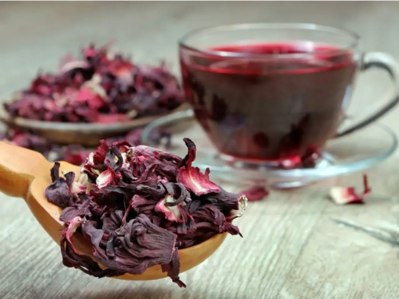 Cucharada de flor de jamaica seca junto a una taza de té rojo vibrante.