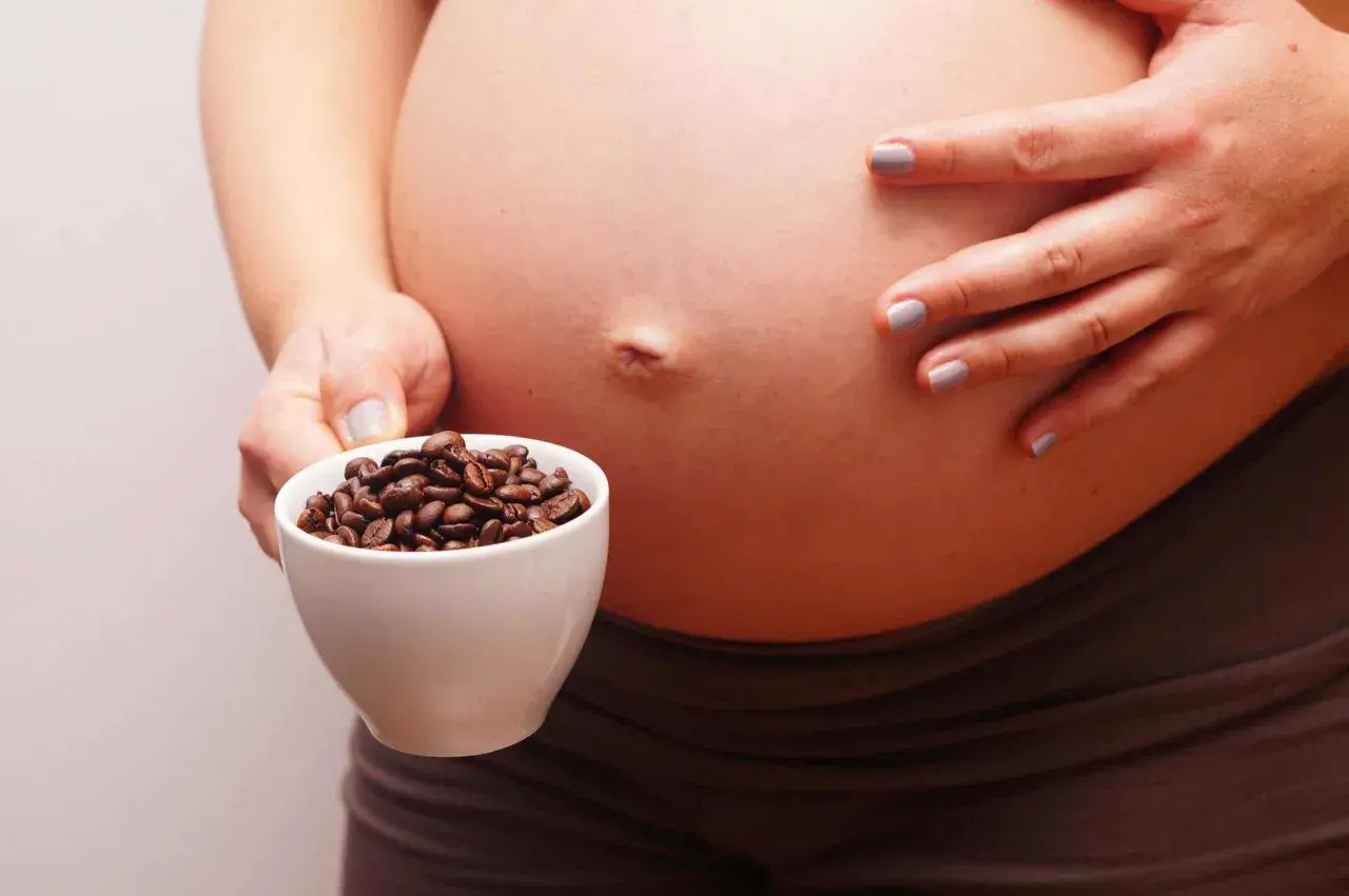 Una mujer embarazada sostiene una taza de granos de café. El café y el embarazo son un tema delicado.