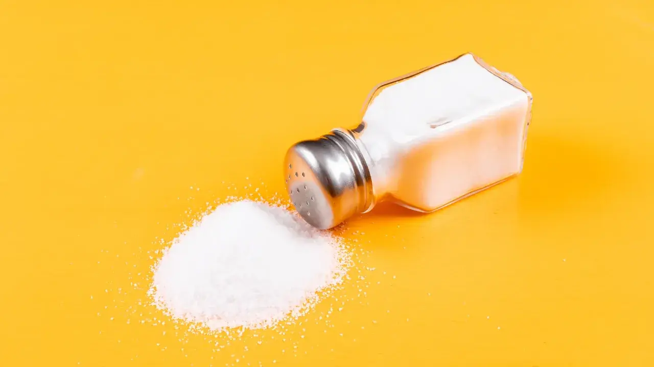 Salero volcado con sal yodada o normal derramada sobre fondo amarillo.