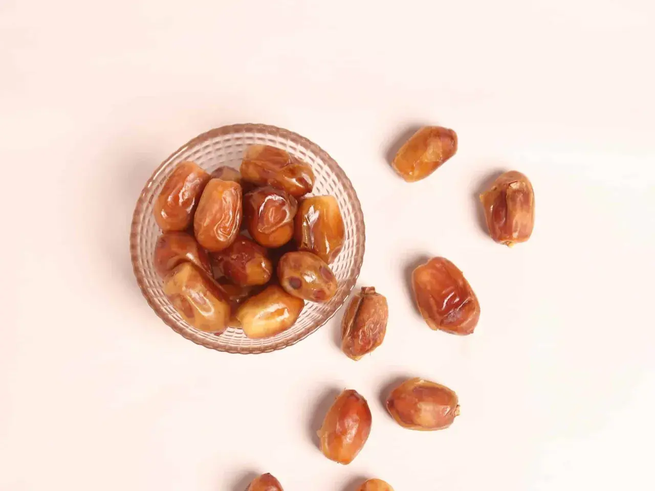 Un cuenco de cristal lleno de dátiles jugosos y otros esparcidos alrededor, destacando sus nutritivas propiedades.