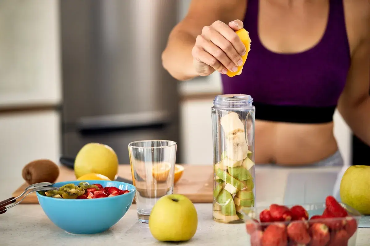 Mujer prepara batido de frutas. Ideal para saber **que tomar para las agujetas** y recuperarse tras el ejercicio.