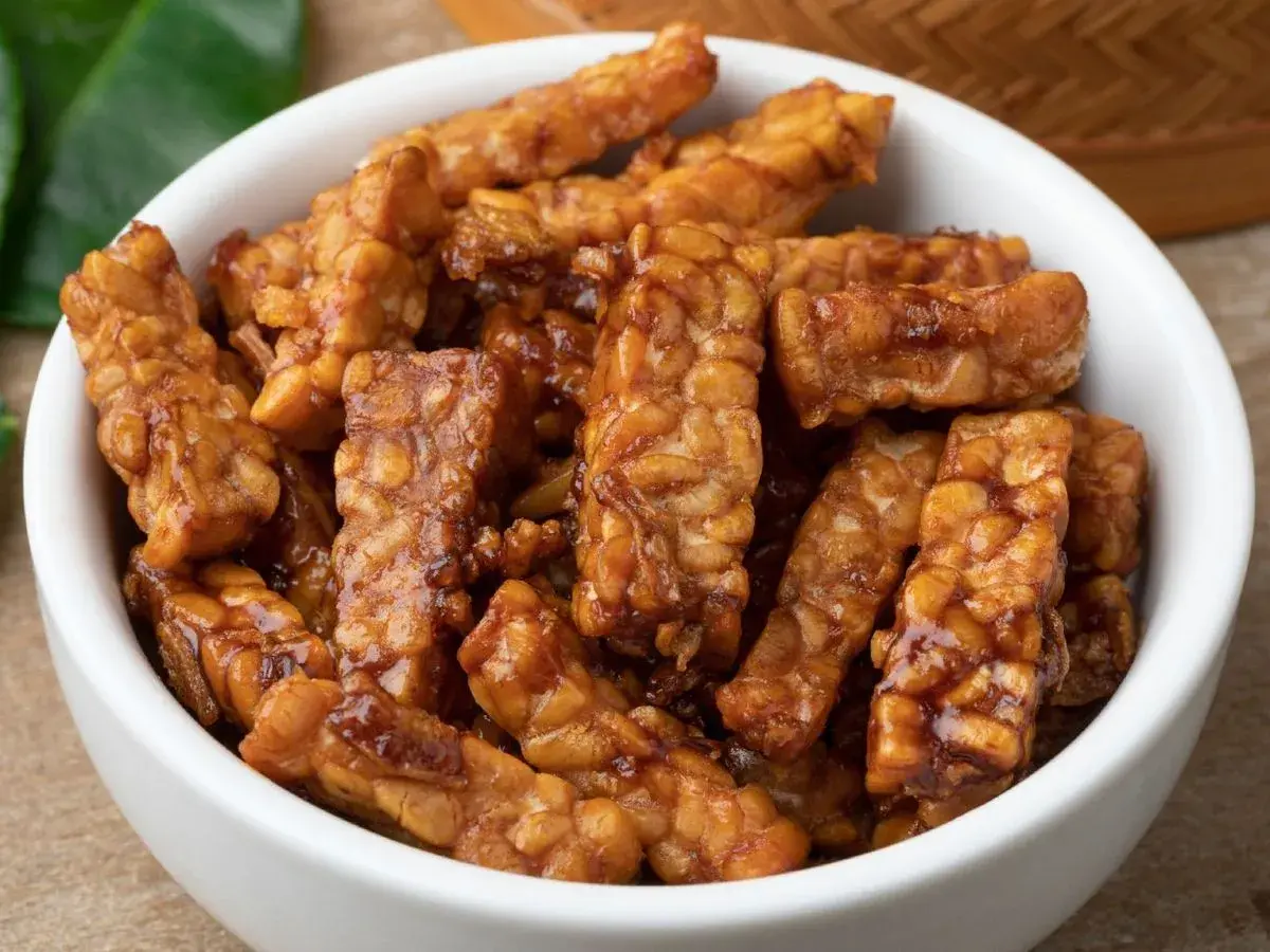 Trozos de tempeh que es, glaseados y dorados, servidos en un cuenco blanco.