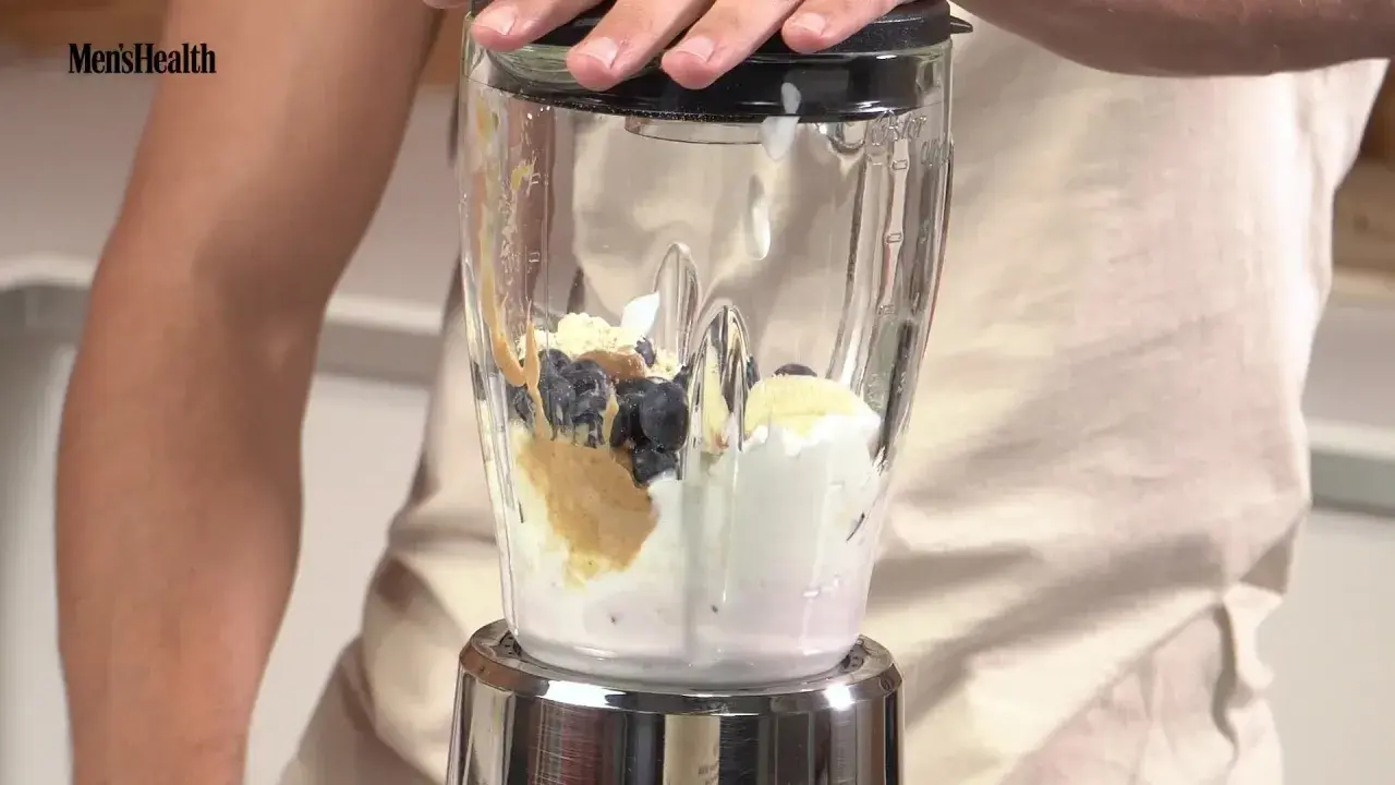 Ingredientes para batidos de proteínas: arándanos, plátano, crema y mantequilla de cacahuete en una licuadora.