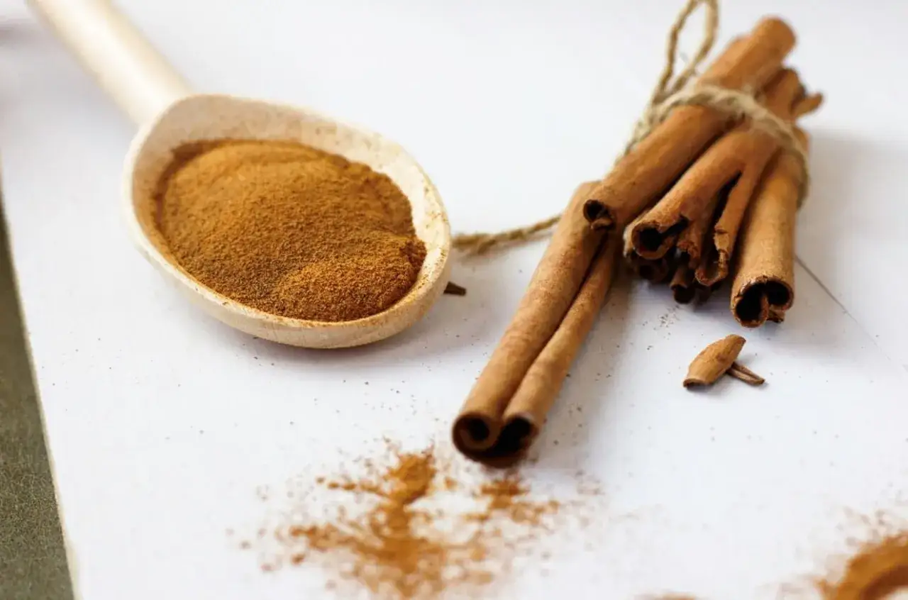 Cucharada de canela molida y ramitas atadas. Descubre los 7 beneficios de la canela molida para tu salud y bienestar.