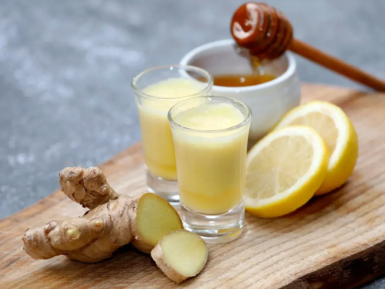 Dos vasos de ginger shot con jengibre fresco, rodajas de lim&oacute;n y miel.