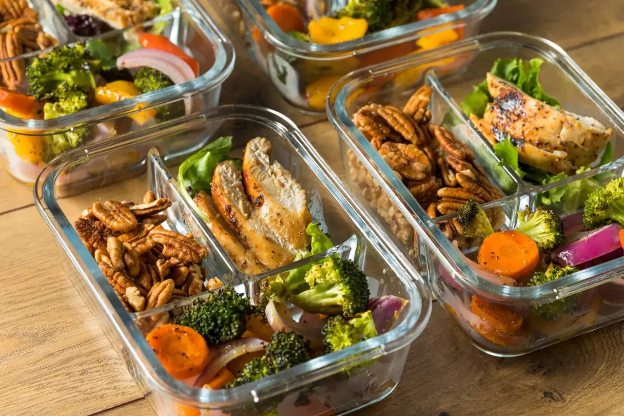 Recetas fitness: recipientes con pollo a la parrilla, br&oacute;coli, zanahoria, cebolla morada y nueces. Comida saludable lista para llevar.