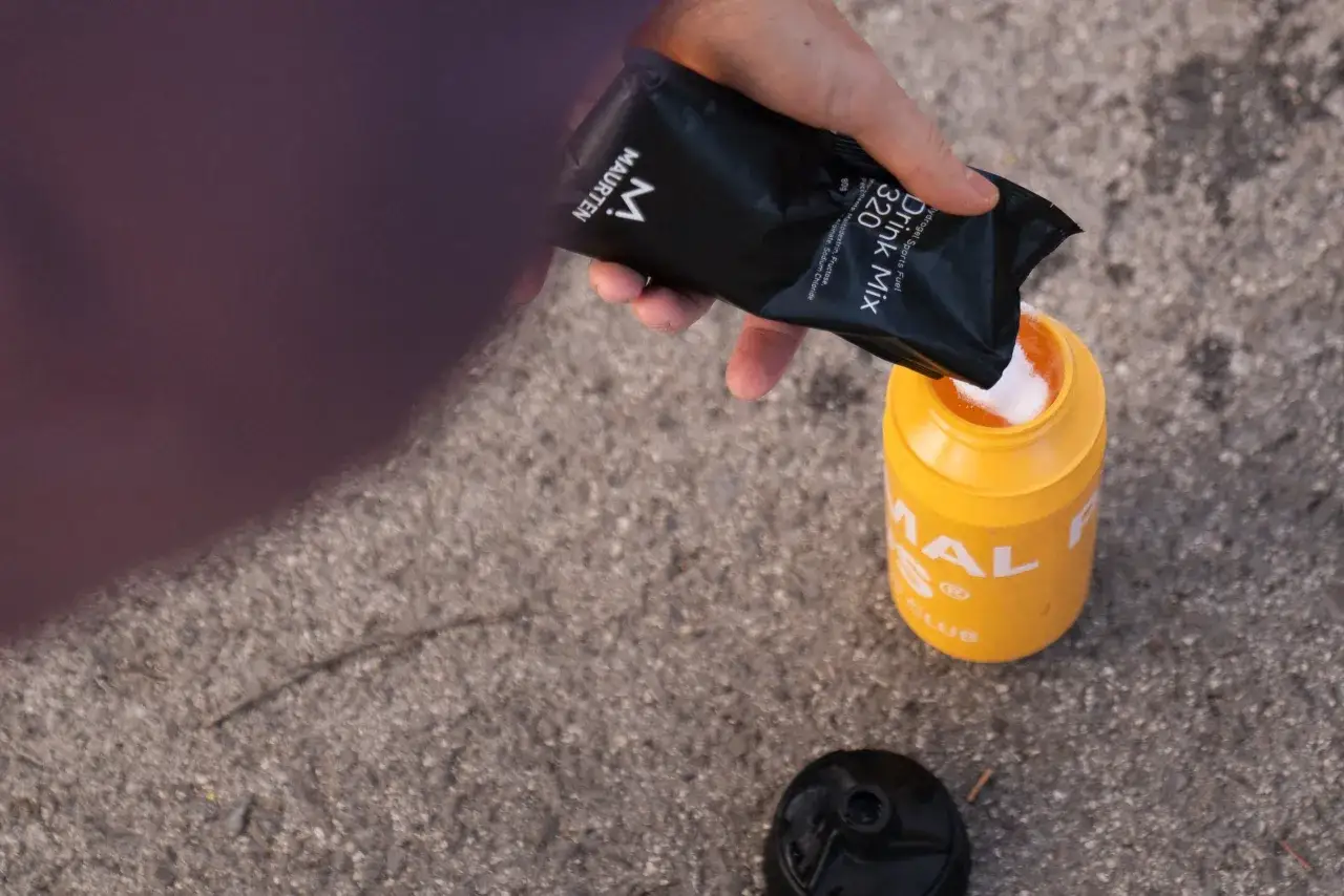 Mano vierte polvo de bebida deportiva Maurten en un bid&oacute;n amarillo. La maltodextrina es mala, pero este producto la usa.