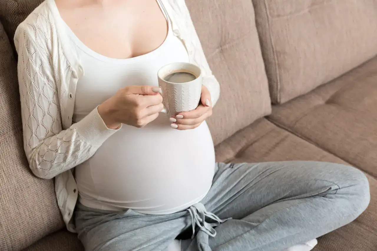 Mujer embarazada sentada en un sofá, disfrutando de una taza de café. El embarazo y el café se combinan en este momento de tranquilidad.