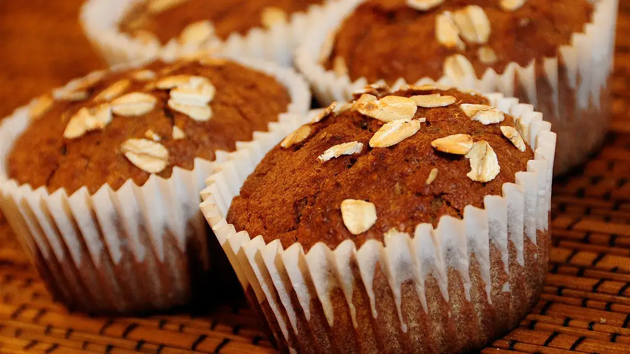 Muffins caseros con salvado de trigo y avena, horneados en papel rizado sobre una superficie de madera.