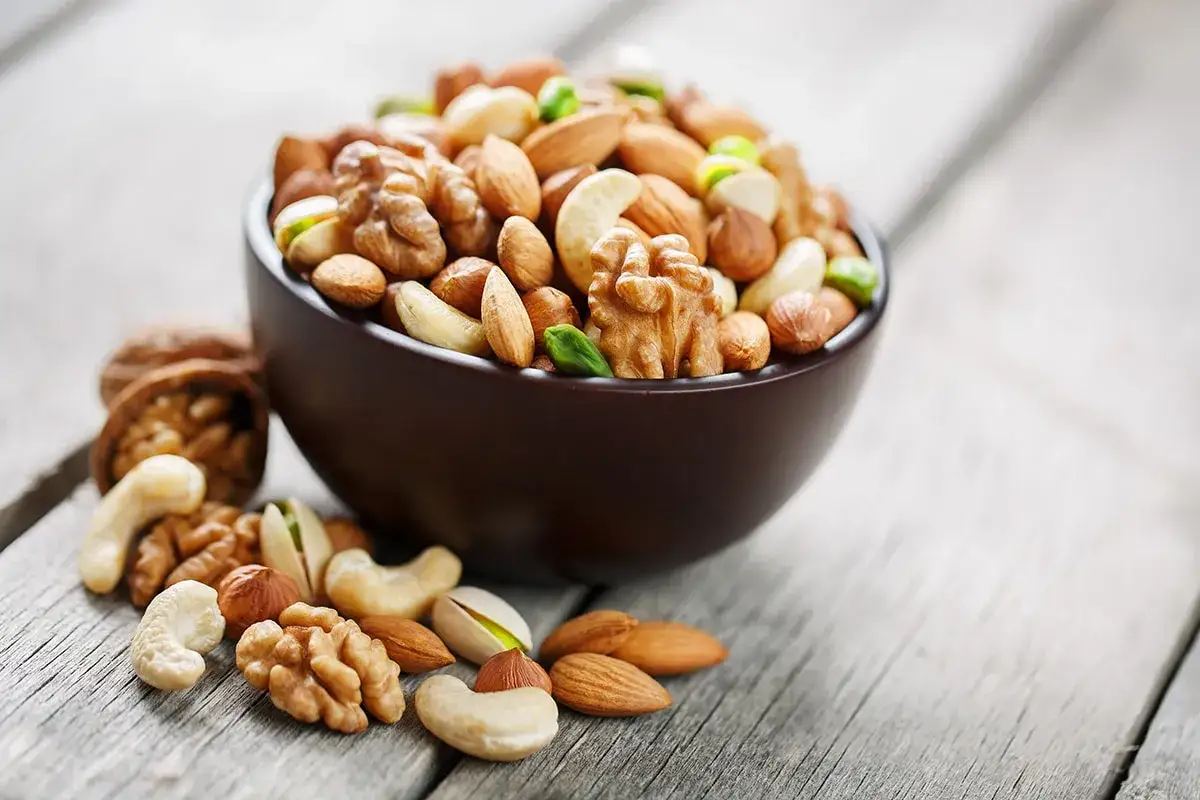 Un taz&oacute;n lleno de frutos secos variados, como nueces, almendras y anacardos, descansa sobre una mesa de madera. &iexcl;Cuidado, los frutos secos engordan!