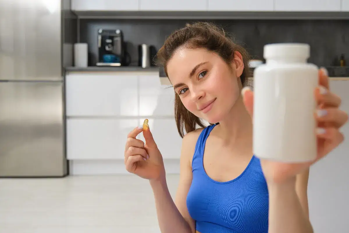 Joven sonriente muestra una cápsula y un frasco, ideal para saber cuándo tomar probióticos y mejorar tu bienestar.