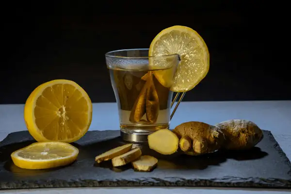 Un vaso de té con limón y jengibre, acompañado de rodajas de limón y trozos de jengibre fresco. Un shot de jengibre para revitalizar.
