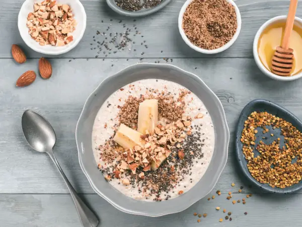 Un tazón de avena con plátano, almendras picadas, semillas de chía y miel. Aprende como tomar avena para un desayuno nutritivo.