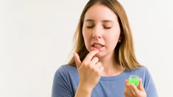 Mujer aplica bálsamo en sus labios cortados, buscando un remedio casero.